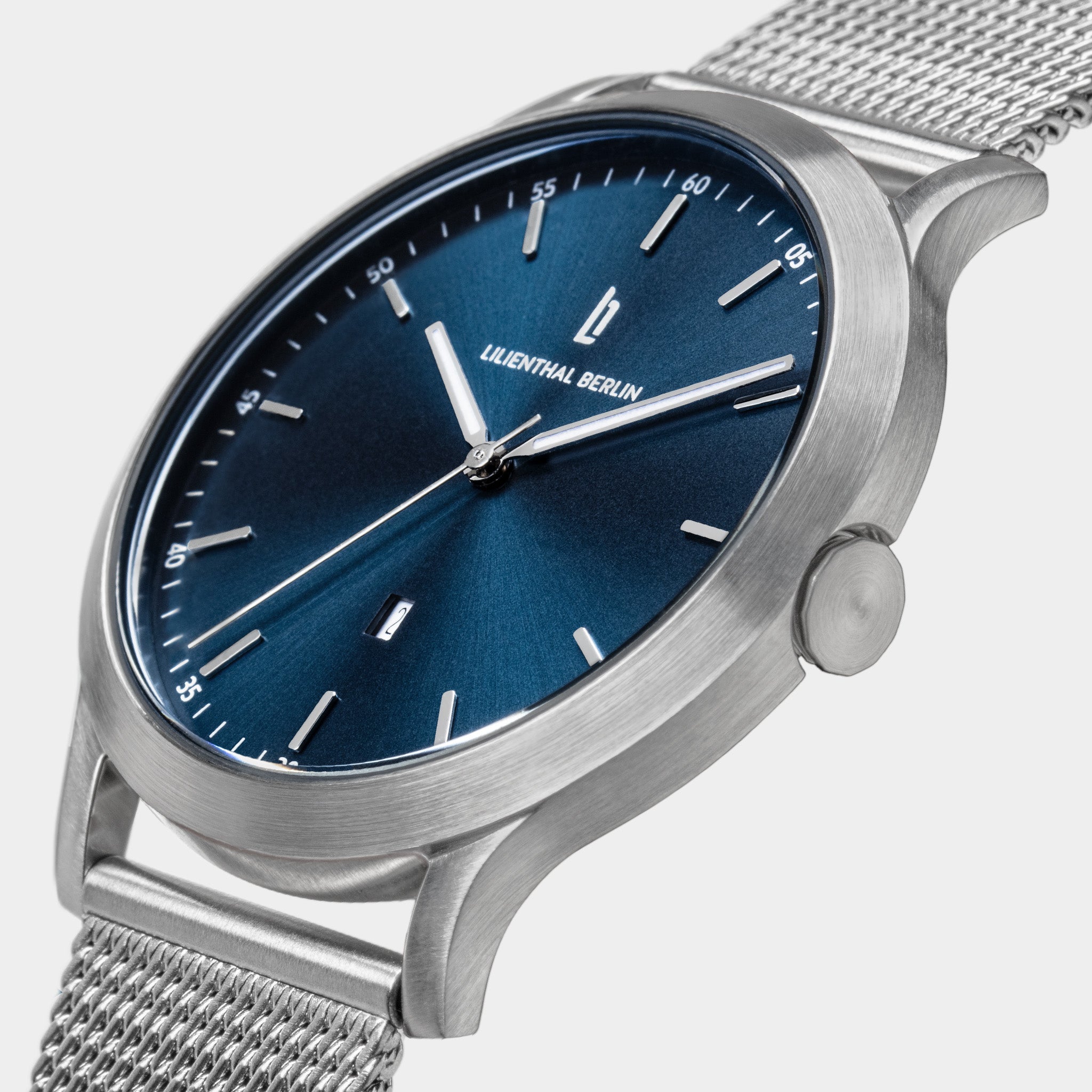 Minimalist silver mesh watch with blue dial and date display on light background