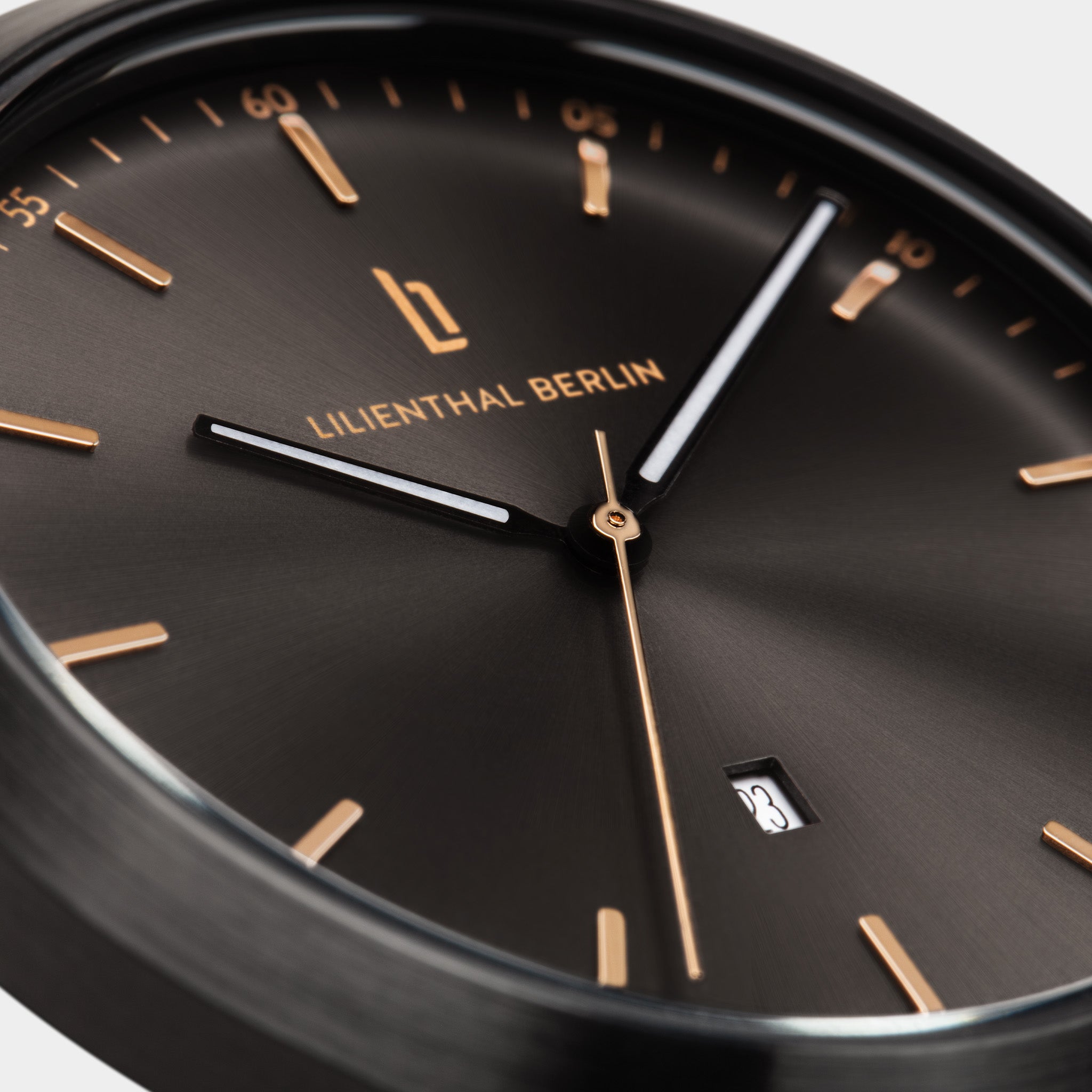 Close-up of minimalist black watch face with gold markers, sleek hands, and date display.