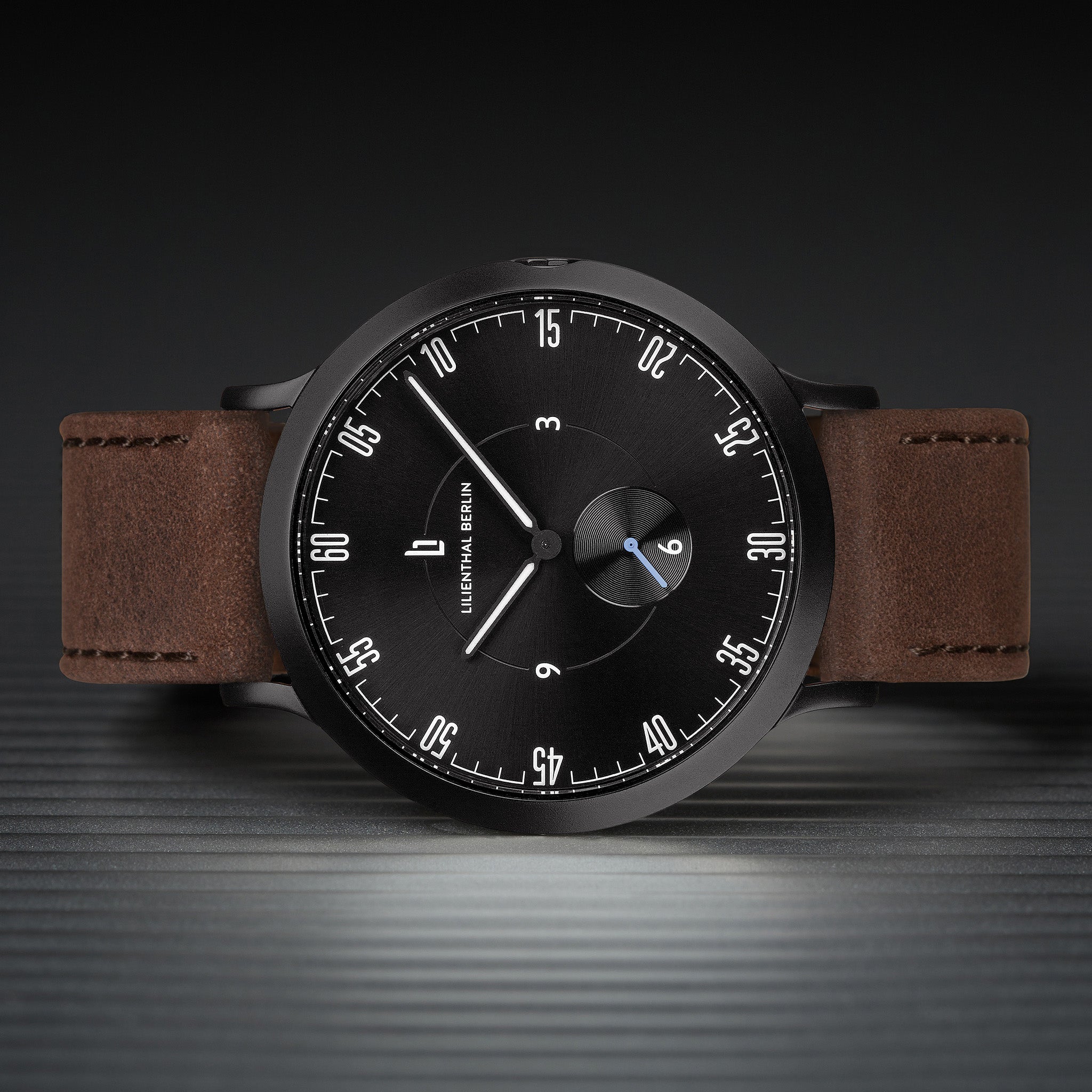 Minimalist black dial watch with brown leather strap on textured surface