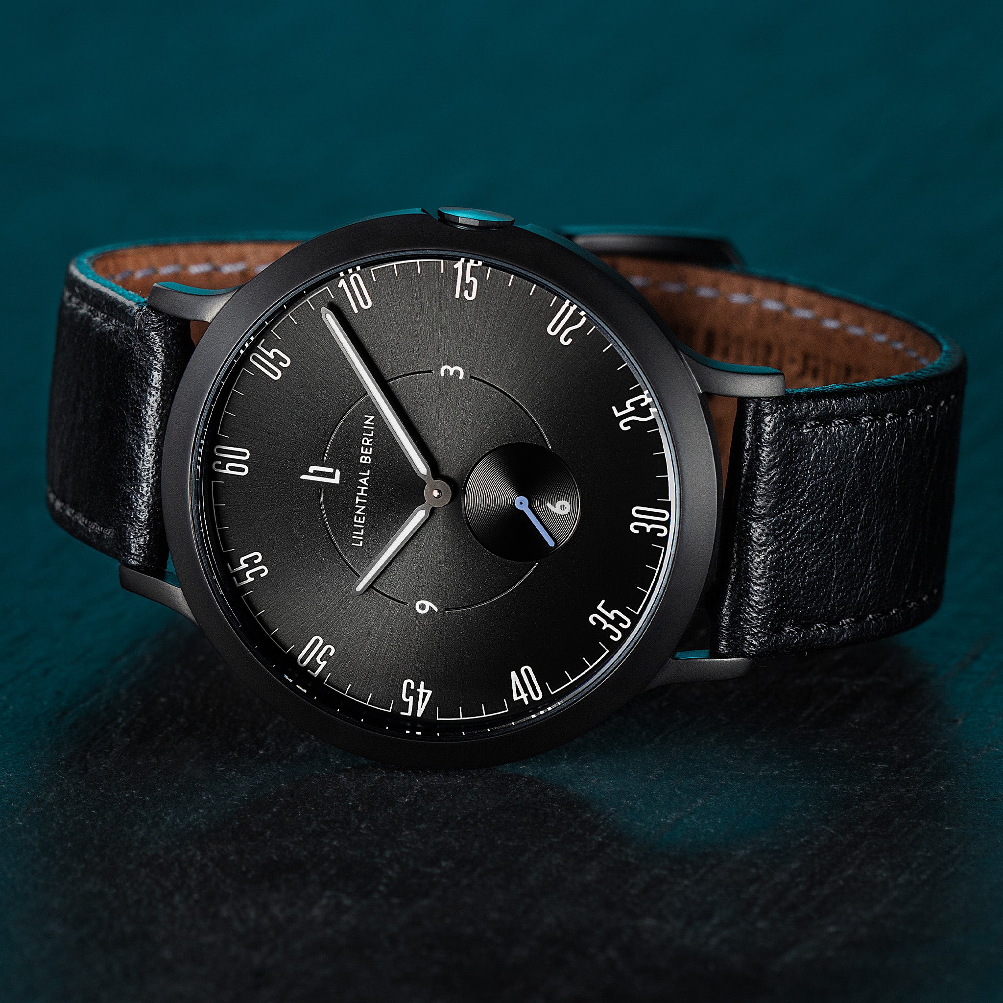 Minimalist black wristwatch with leather strap against dark textured background