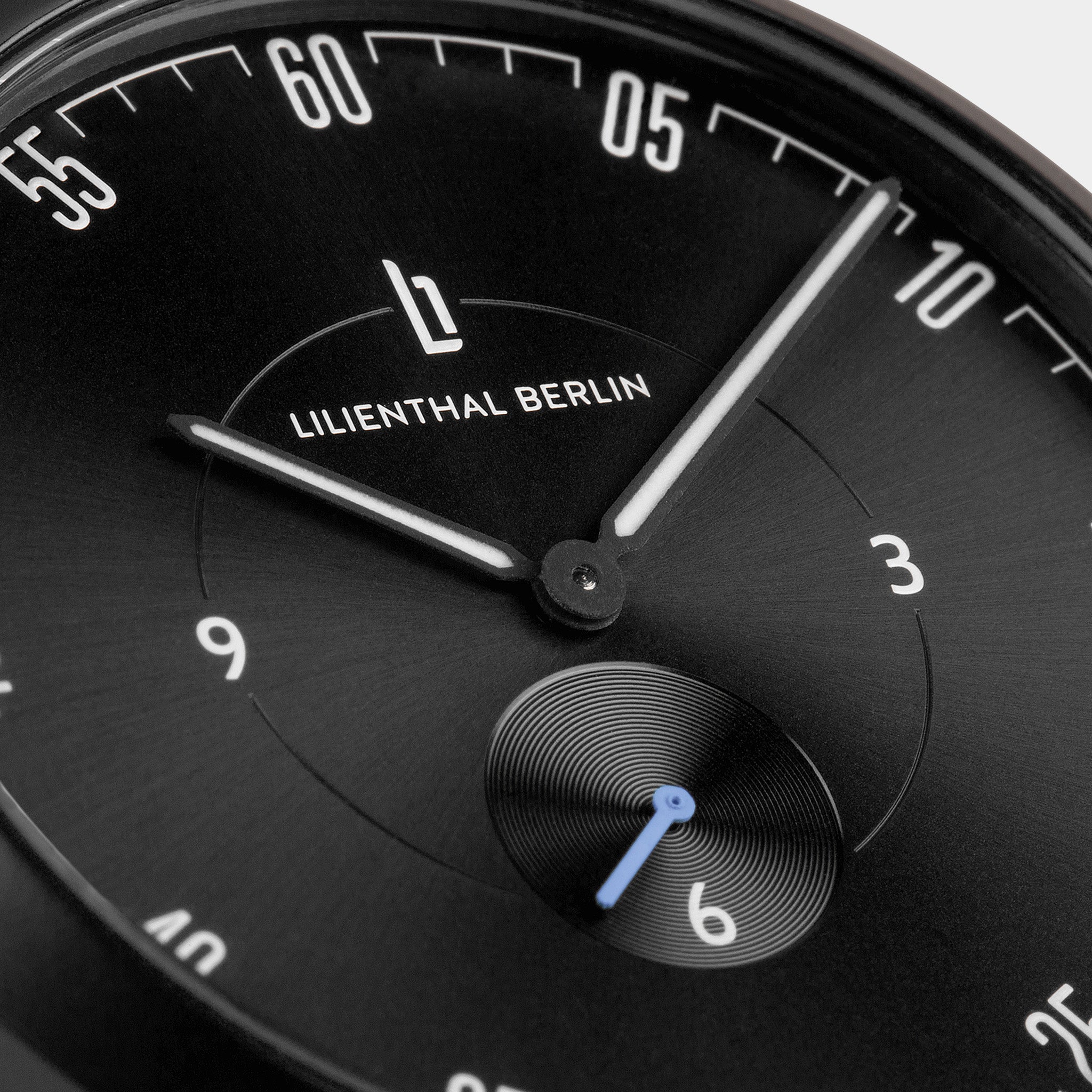 Close-up of a modern black watch face with minimalist white markers and blue second hand.