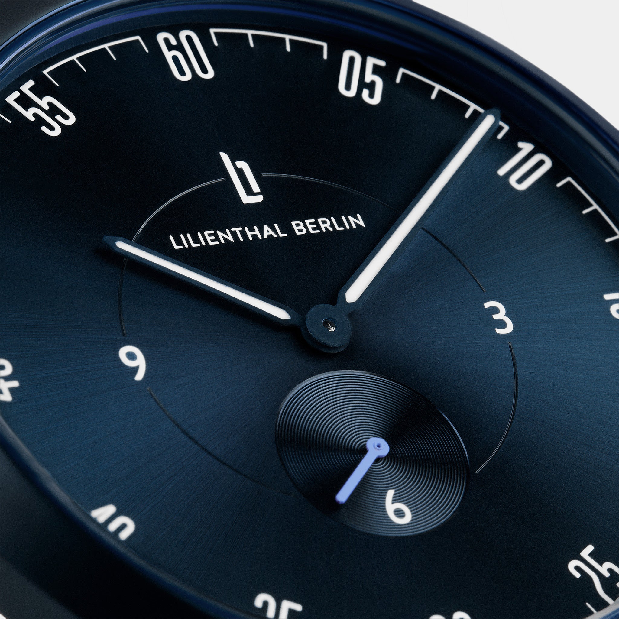 Close-up of a minimalist blue watch face with luminous hands and subdial.