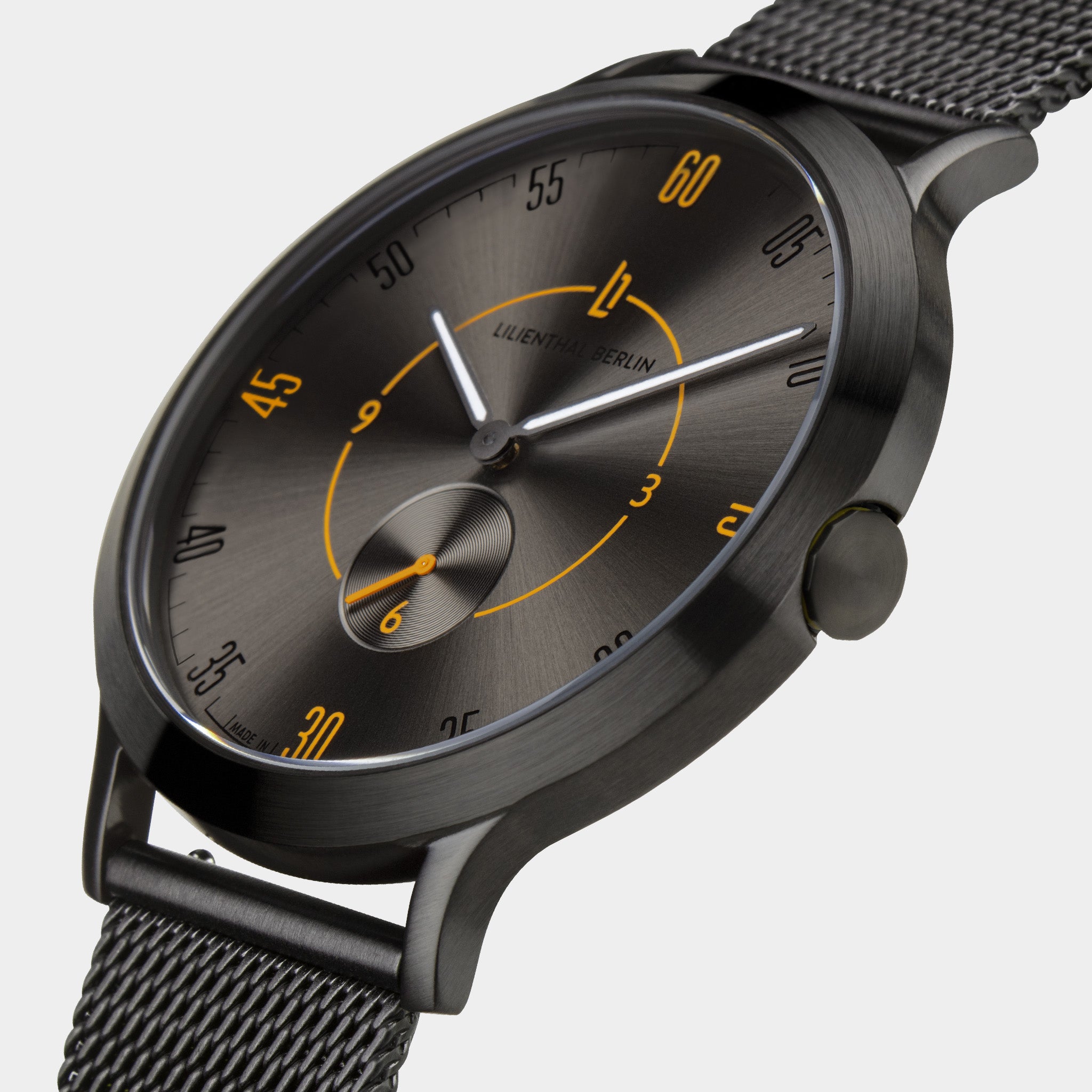 Close-up of a modern black mesh strap watch with a dark grey dial and yellow accents.