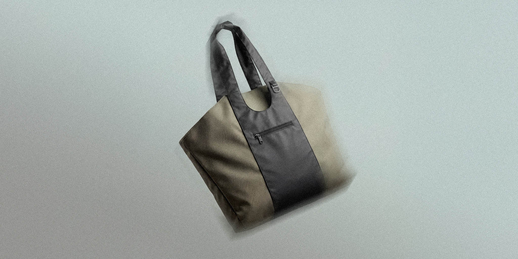 Modern beige and black tote bag with front zipper pocket and dual handles on grey background