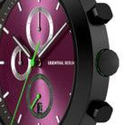 Close-up of a modern chronograph watch with a metallic magenta dial, black case, and green accents.