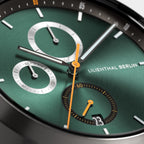 Close-up of a green chronograph watch face with orange hands and detailed sub-dials