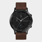 Black chronograph watch with brown leather strap and date display on white background