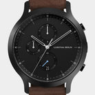 Black chronograph watch with subdials, date display, and brown leather strap
