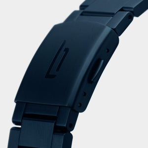 Close-up of a matte black metal watch clasp with engraved logo on a linked bracelet