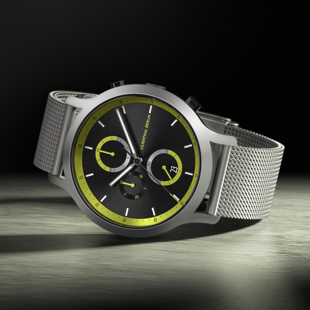 Modern chronograph watch with black and yellow dial, silver mesh strap, and bold accents