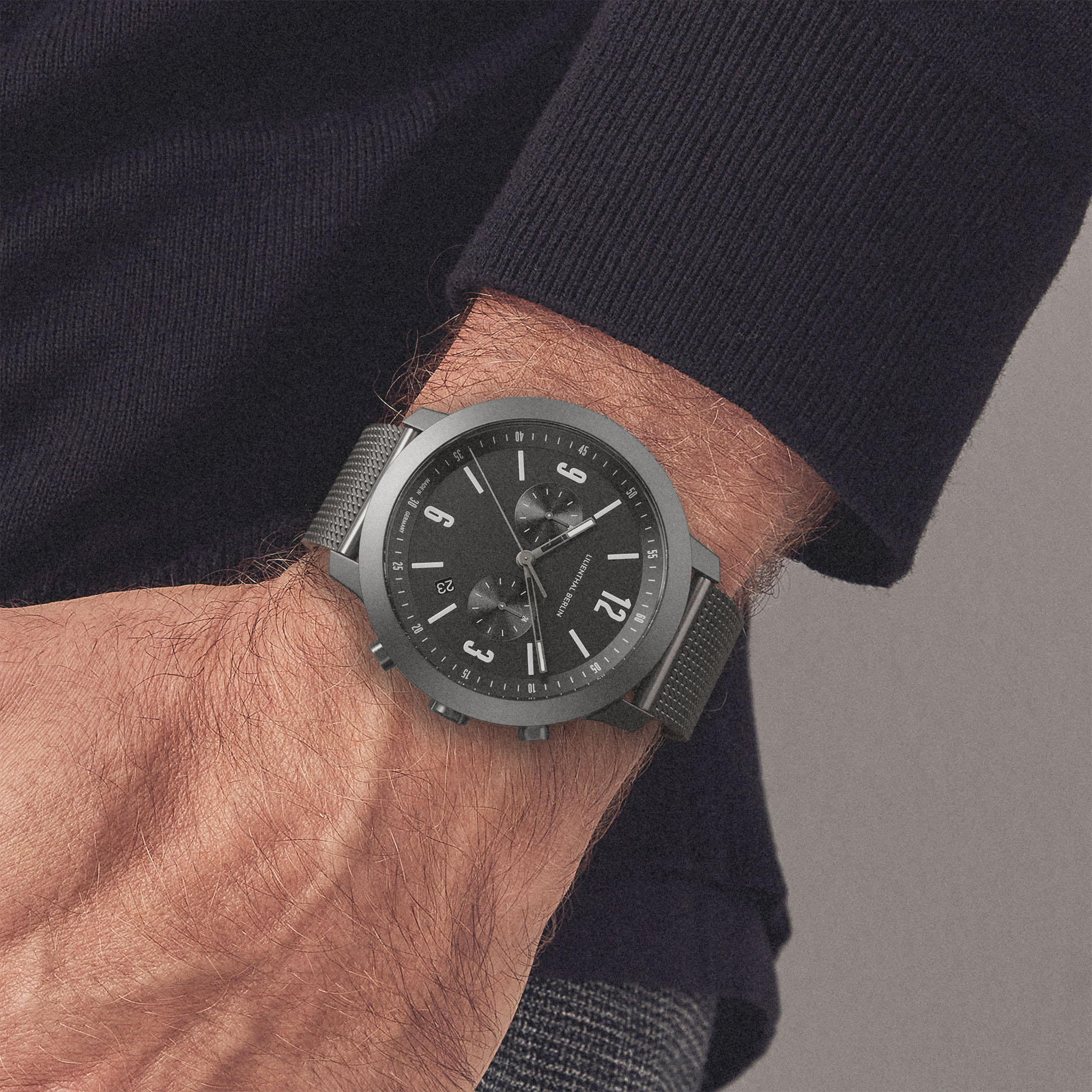 Man wearing a modern black chronograph wristwatch with mesh strap and black dial