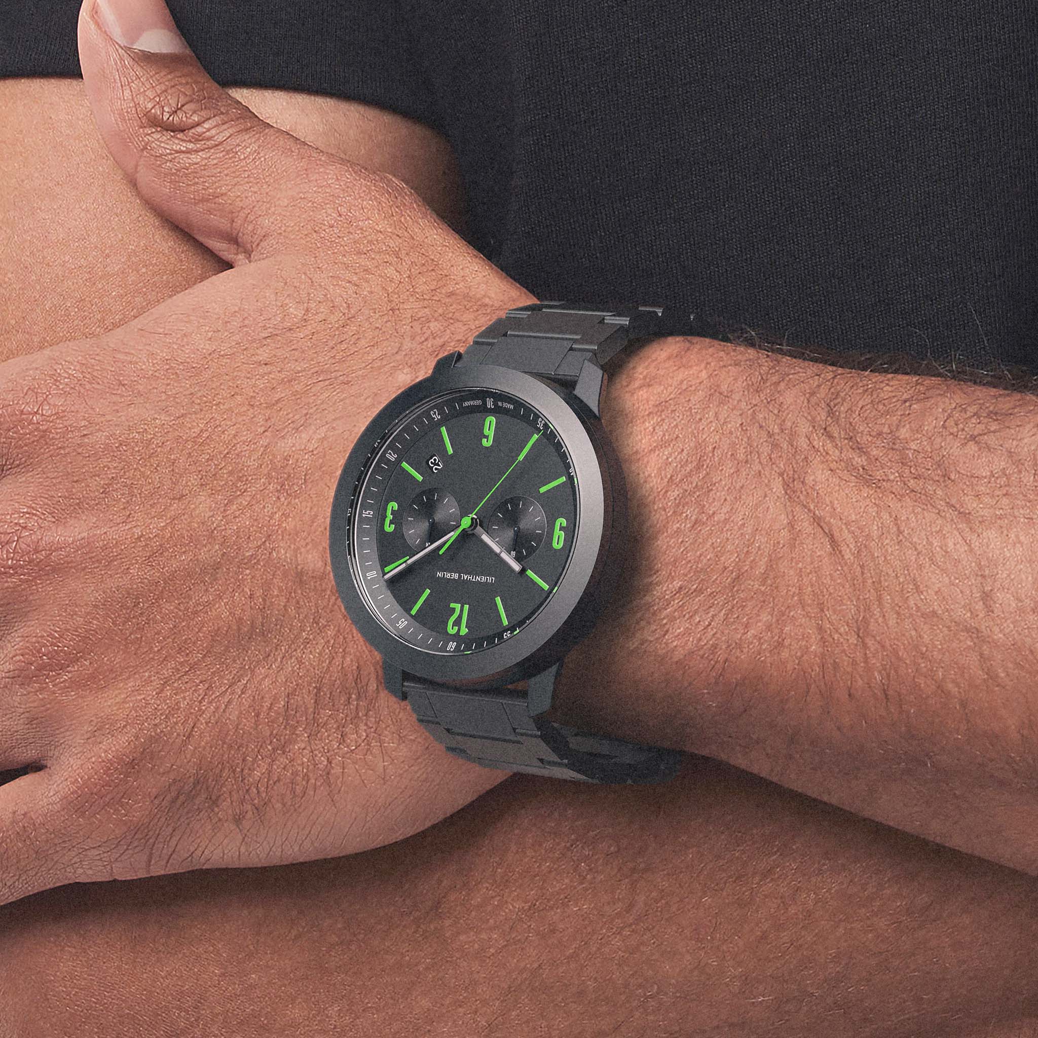 Black wristwatch with green accents and metal band on a person's wrist