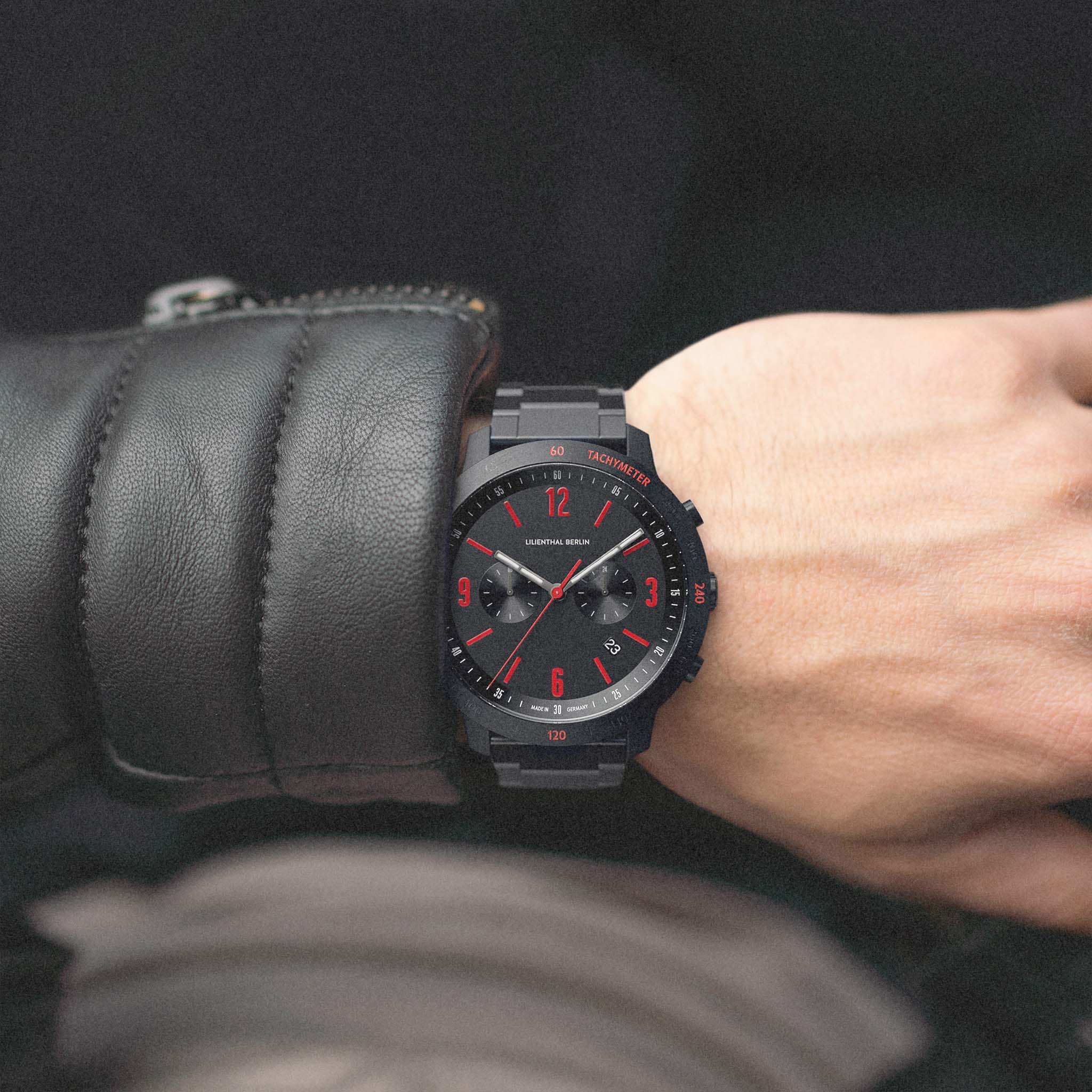 Black chronograph watch with red accents and metal band on wrist, urban style fashion accessory