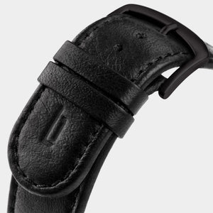 Close-up of a black leather watch strap with matte black buckle and stitched detailing