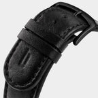 Close-up of black leather watch strap with matte black buckle on light background