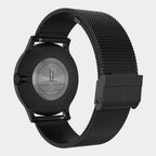 Black stainless steel wristwatch with mesh strap, showing engraved case back and clasp