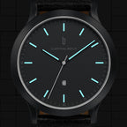 Minimalist black analog watch with luminous blue hour markers and date display