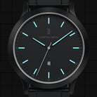 Black minimalist wristwatch with blue luminous markers, metal band, and date display