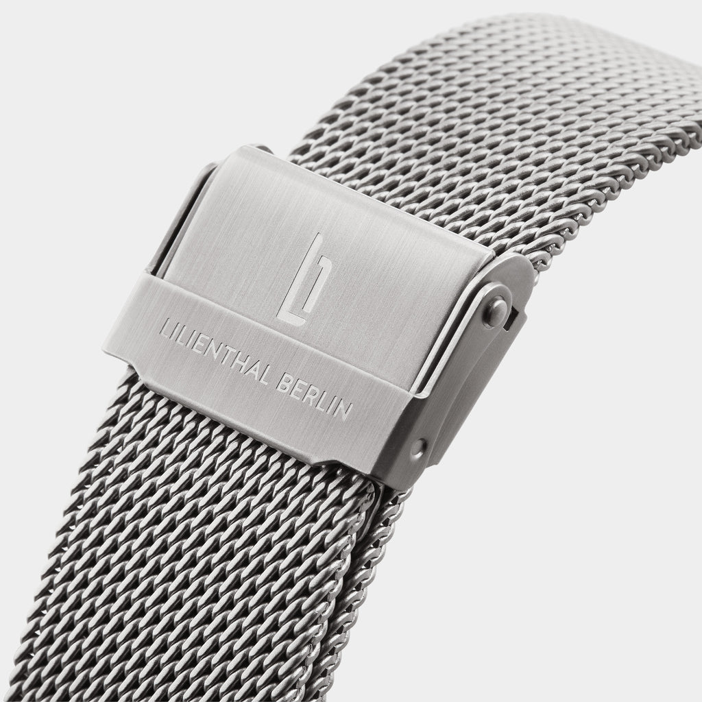 Close-up of stainless steel mesh watch strap with engraved clasp on white background