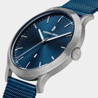 Minimalist blue dial wristwatch with silver case and blue mesh strap, close-up view