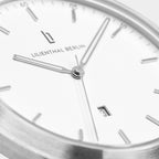 Close-up of a minimalist silver watch face with date display and white dial.