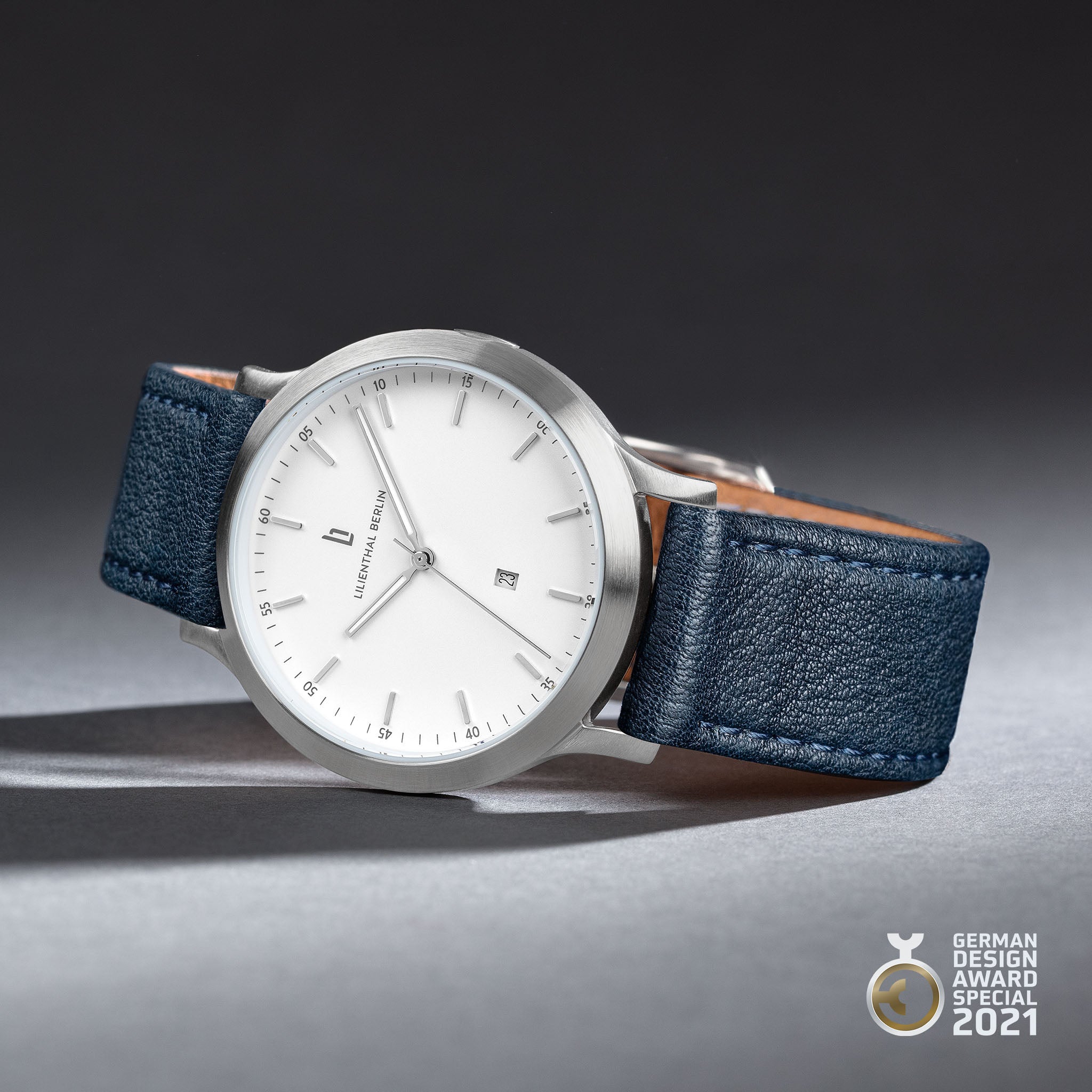 Minimalist silver wristwatch with white dial, blue leather strap, and German Design Award 2021 badge