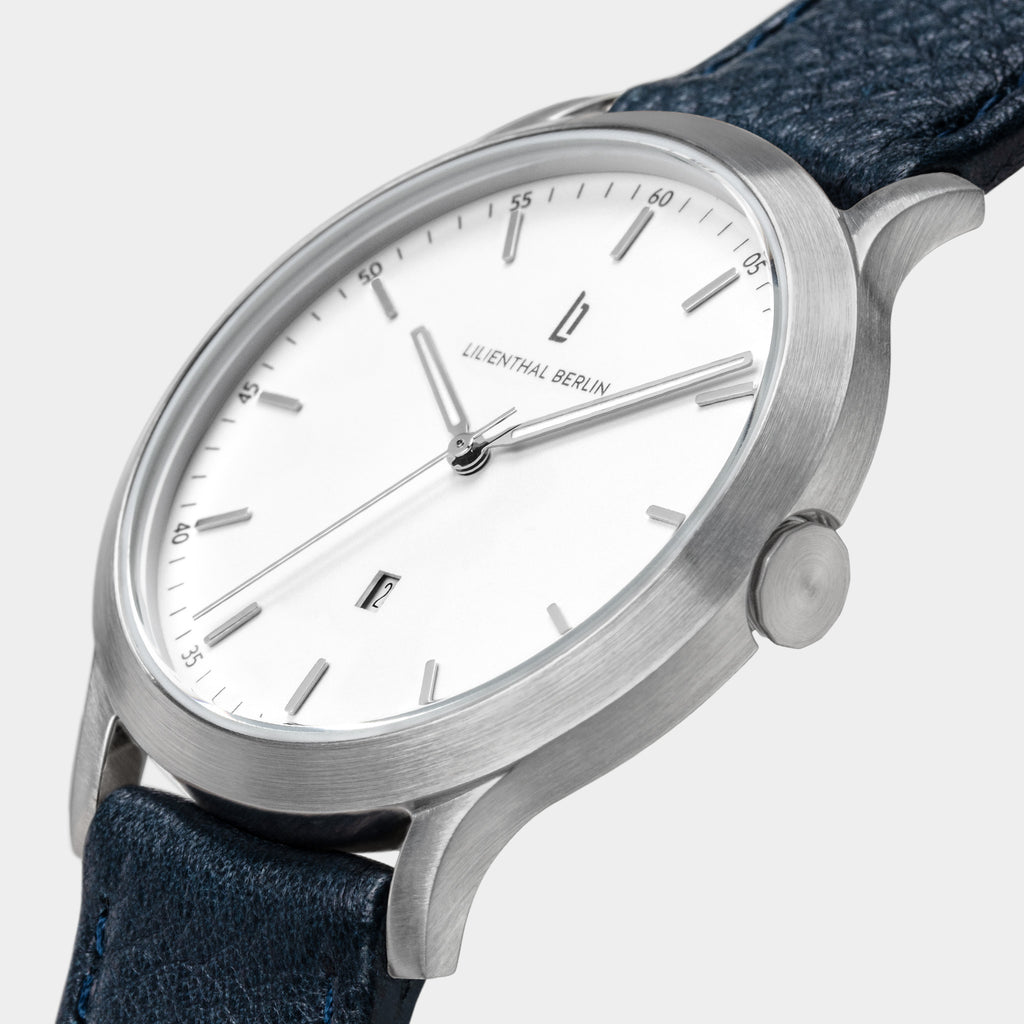 Minimalist silver wristwatch with white dial, date window, and dark textured leather strap