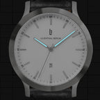 Minimalist silver wristwatch with white dial, luminous blue hands, and date display