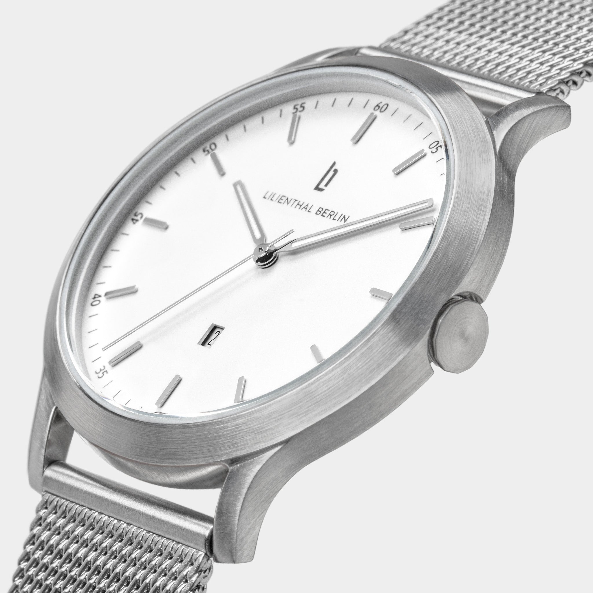 Minimalist silver mesh wristwatch with white dial and date window on a light background
