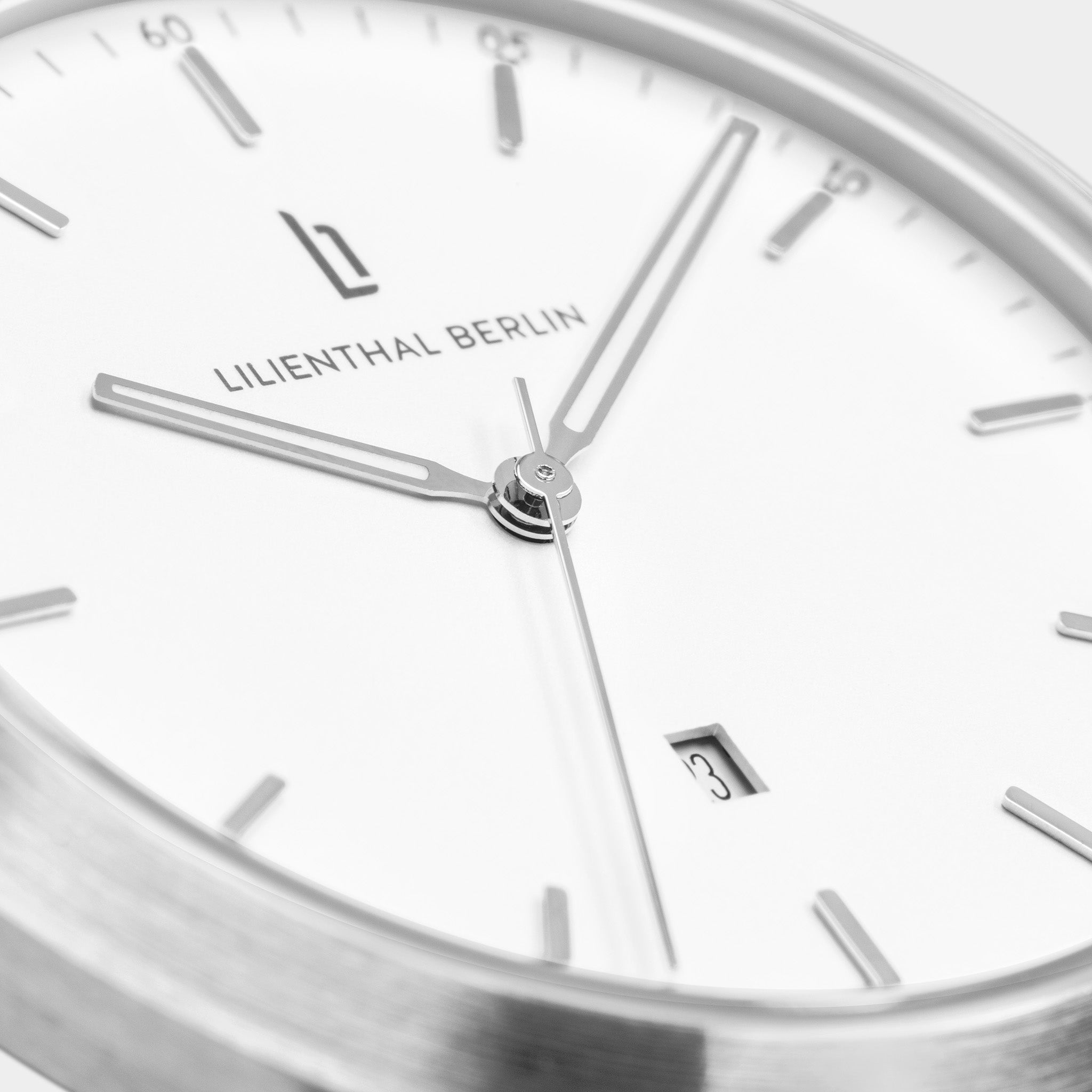 Minimalist silver watch with white dial, date window, and slim hands, close-up view