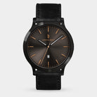 Men's black leather strap watch with dark sunburst dial, gold-tone markers, and date window