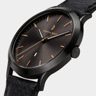 Minimalist black wristwatch with rose gold accents and black leather strap, close-up view