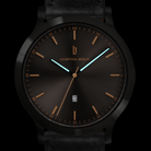 Minimalist black watch with gold hour markers, blue hands, date window, and leather strap