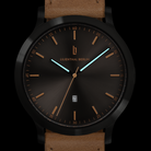 Modern black watch with brown leather strap, minimalist dial, gold accents, and date display