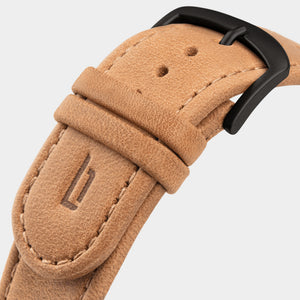 Close-up of a tan leather watch strap with black buckle and stitched edges