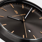Close-up of a minimalist black watch face with gold hour markers and visible date display.