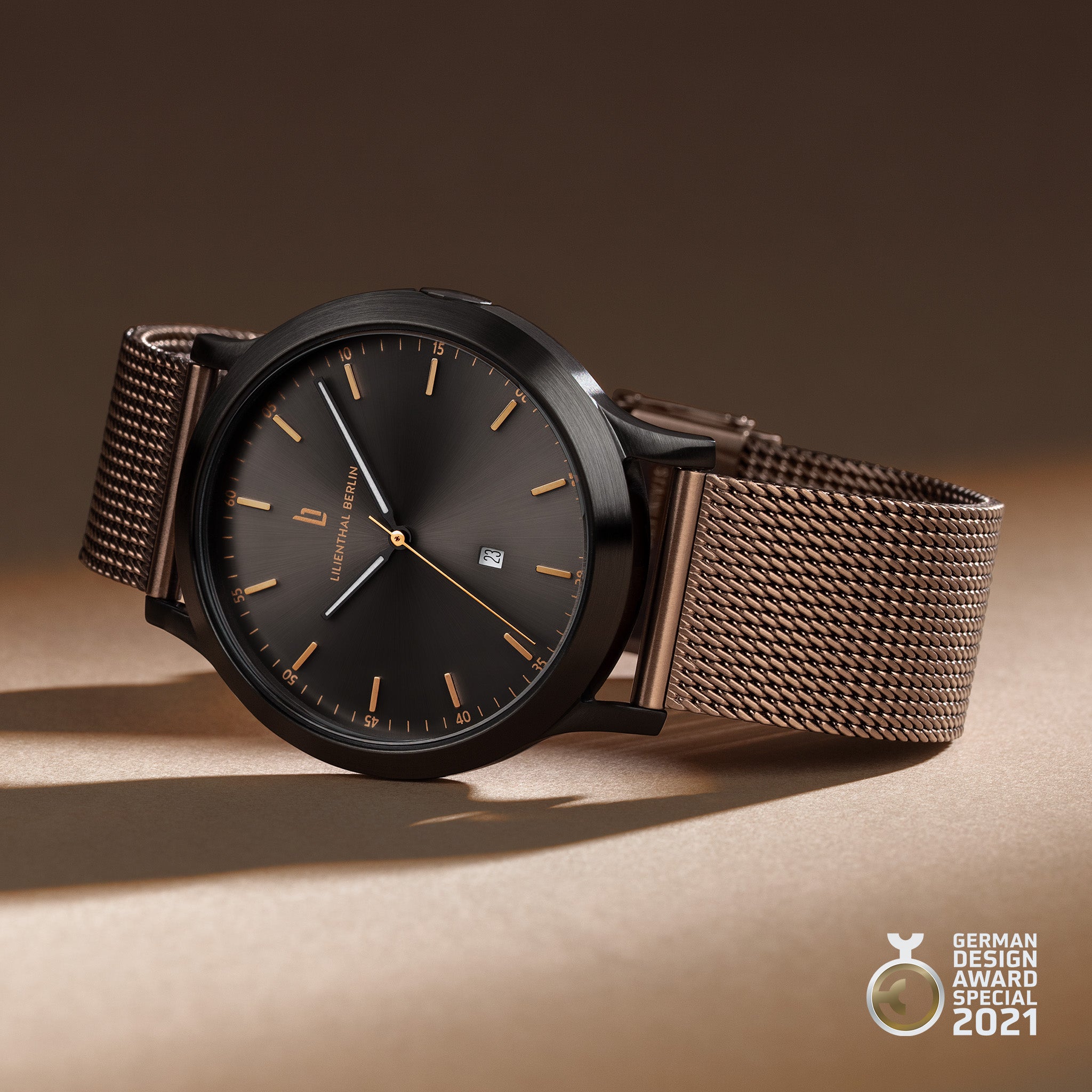 Minimalist brown mesh strap designer watch with black dial, gold accents, and date window