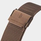 Close-up of bronze mesh watch strap with engraved clasp and modern design.