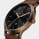 Elegant bronze and black wristwatch with minimalist design and brown leather strap