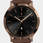 Minimalist wristwatch with black dial, bronze case, brown leather strap, and date display