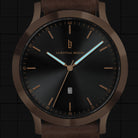 Minimalist black and bronze analog wristwatch with brown leather strap and date display