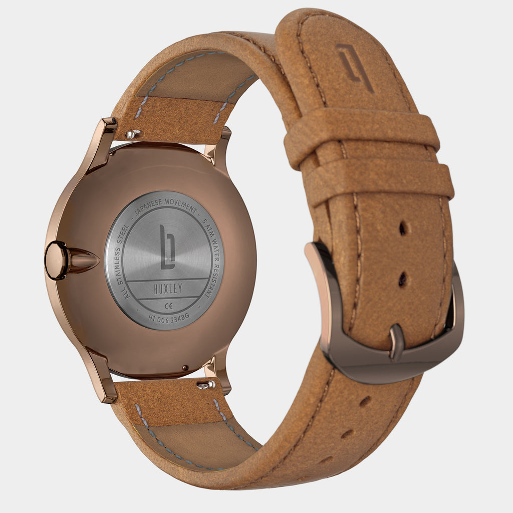 Close-up of a rose gold watch case with tan leather strap and engraved backplate