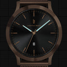 Black and bronze minimalist watch with date display and mesh band, close-up dial view