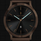Black and bronze minimalist watch with date display and mesh band, close-up dial view