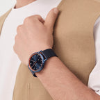 Stylish blue wristwatch with mesh strap and orange bezel on man's wrist in beige vest