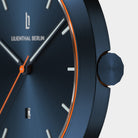 Close-up of a modern blue watch face with orange accents, sleek hands, and minimalist markers