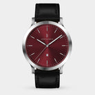 Minimalist wristwatch with a red dial, silver case, and black leather strap on white background