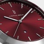 Close-up of red minimalist wristwatch with silver markers and date display
