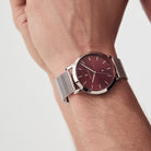 Minimalist silver mesh watch with burgundy dial on wrist, modern stylish accessory