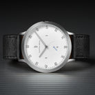 Minimalist silver watch with white dial, black leather strap, and sleek hour markers